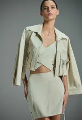 Chaqueta cropped color beige con cuello clásico, cierre frontal con botones, mangas largas anchas y bolsillos frontales con solapa y hebillas decorativas.