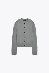 Chaqueta corta de punto gris jaspeado, con cuello redondo y cierre frontal de botones oscuros.