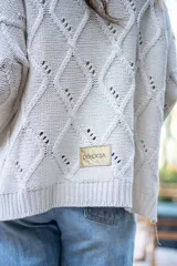 Saco tejido de punto con diseño de ochos y trenzas, color negro. Presenta cuello estilo camisero, cierre frontal con botones tipo joya, mangas holgadas y silueta oversize.