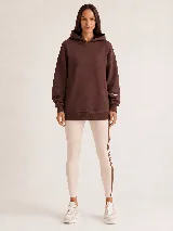 Hoodie Trena de frisa color marrón chocolate, con moldería oversize, hombros caídos, capucha con cordones ajustables y bolsillo tipo canguro. Presenta puños y ruedo de rib elástico, y detalles de bordado en la manga.