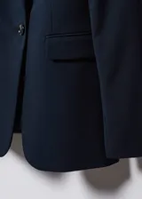 Blazer entallada de corte sastre, con solapas de muesca, hombros estructurados y cierre frontal de un botón. Presenta dos bolsillos de ribete delanteros, pinzas para un ajuste preciso y abertura posterior.