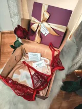 Caja de regalo artesanal color bordó con moño dorado, diseñada como experiencia de lujo para presentar un conjunto de lencería. Incluye elementos de regalo adicionales como perfume, rosa natural y dulces.