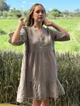 Vestido corto de lino color beige claro, con cuello mao, escote con botones de nácar, mangas tres cuartos con volados y ruedo con volado.