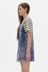 Mono enterito corto de denim azul con lavado ácido, corte oversized, tirantes regulables, bolsillo plaqué en el pecho y ruedo desflecado.