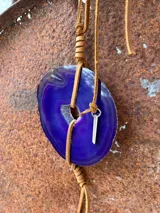 Collar con dije de piedra ágata blanca y marrón, con forma circular irregular y agujero en el centro. El dije está sujeto con un cordón fino de cuero marrón.