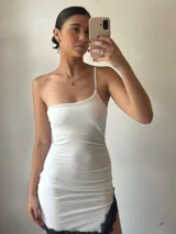 Minivestido blanco ajustado al cuerpo, de un solo hombro y con terminación de encaje negro en el ruedo.