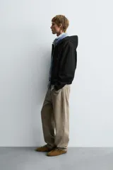 Cazadora negra de algodón con efecto lavado, corte relajado y capucha ajustable. Presenta cierre frontal de cremallera, bolsillos frontales tipo canguro y elásticos en puños y bajo.