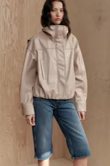 Chaqueta color beige de efecto piel, con cuello subido, manga larga con puño y bolsillos laterales. Tiene forro interior y bajo elástico. Cierre frontal con cremallera y botones a presión ocultos por solapa.