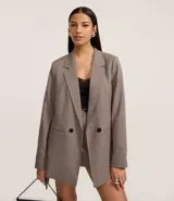 Blazer de sastre alargado, cruzado con doble botón, de manga larga y cuello solapa. Presenta un estampado de cuadros pata de gallo (pied de poule) en tonos marrones y beige.