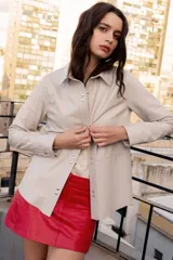 Camisa de cuero color verde oliva, con cuello camisero, cierre frontal mediante broches metálicos y mangas largas con puños abotonados.