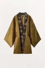 Kimono reversible de corte holgado con escote en pico y mangas anchas por debajo del codo. Un lado presenta un acabado texturizado en color bronce, mientras que el otro lado muestra un estampado floral sobre fondo oscuro. Incluye cierre frontal con lazada fina.