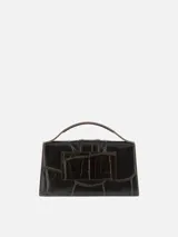 Bolso Le Grand Bambino de Jacquemus confeccionado en cuero de ternera con estampado efecto cocodrilo en color marrón oscuro. Presenta una silueta estructurada, solapa frontal con cierre magnético y tira vertical, asa superior rígida y correa ajustable y desmontable. Incluye detalles metálicos dorados con el logotipo de la marca en el frente.