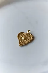 Collar con dije de corazón en acero quirúrgico, con textura irregular y relieve, montado sobre un tiento encerado negro.