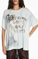 Camiseta de algodón en tono gris claro con efecto desgastado y lavado. Presenta un diseño gráfico frontal con la frase 'If it's meant to be then it will be' y una ilustración de un castillo, con detalles en pedrería o glitter. Posee un corte relajado y mangas cortas.