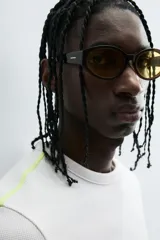 Camiseta de corte relajado, color gris claro, confeccionada en tejido con estructura waffle. Presenta cuello redondo y manga corta, con costuras decorativas en contraste color dorado que recorren los laterales y los hombros.