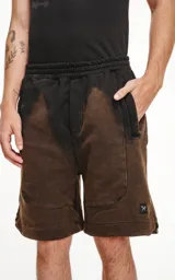 Bermuda de algodón rústico color negro con efecto acid wash/oxidado, corte oversize y cintura elástica. Presenta bolsillos laterales con cierre y un pequeño logo bordado en la parte inferior derecha.