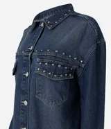 Camisa de jean estilo overshirt con corte oversized, cuello clásico y mangas largas. Presenta cierre frontal con botones, dos bolsillos delanteros con solapa y aplicación de tachuelas metálicas en el cuello y la parte superior del pecho.