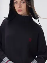 Pullover de punto color negro con cuello tortuga, mangas largas con puños acanalados en gris y detalle de logo bordado en el pecho.