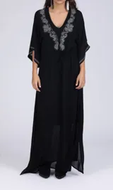 Vestido largo negro con bordado floral en el escote y mangas tres cuartos con aberturas. Tiene corte amplio y lazo ajustable en la cintura.