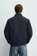 Sobrecamisa de corte regular fit en tejido técnico negro resistente al agua, con cuello estilo bomber en rib elástico, cierre frontal de cremallera y bolsillos plastrón con solapa en la cadera.