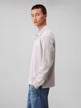 Chomba de manga larga Calvin Klein color gris, confeccionada en tejido jersey grueso aterciopelado de algodón. Cuenta con cuello clásico, cierre frontal con tres botones y logo de la marca bordado en relieve en el pecho.