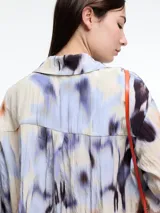 Camisa oversized de manga larga confeccionada en viscosa crinkled con estampado de manchas en tonos blanco, negro y marrón. Presenta bolsillos frontales grandes, tajos laterales y un largo extendido en la espalda.