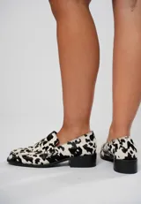Mocasín de cuero con pelo y estampado de vaca en blanco y negro. Presenta horma cuadrada, diseño enrejillado en la capellada y taco bajo de 4,5 cm.