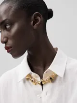 Collar con cinta de poliéster negra que se ata con un lazo y adorno central de piezas metálicas torneadas con acabado dorado.