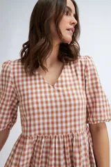 Vestido midi con estampado a cuadros color terracota y crudo, escote en V y mangas abullonadas cortas. Tiene corte imperio y falda escalonada.