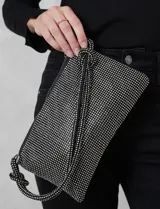 Cartera de strass color negro, con cierre metálico y bolsillo interior. Incluye una correa de mano trenzada y un cierre de cremallera.
