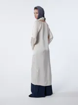 Vestido largo color crema, tipo túnica, confeccionado en crepé de satén de seda teñida en prenda. Tiene escote en pico con costura y ligeros fruncidos bajo el busto, líneas rectas y mangas acampanadas.