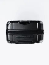 Valija rígida de viaje color negro con diseño geométrico en relieve, manija telescópica y cuatro ruedas con giro de 360°.