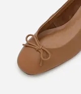 Zapato femenino de cuero color tostado, estilo muñeca con punta redondeada y detalle de mini lazo en la parte superior. Cuenta con tacón bloque de altura mediana.