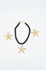 Set compuesto por un collar de cordón negro trenzado con dije de estrella de mar dorada y un brazalete a juego con diseño de estrella de mar dorada.