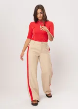 Pantalón beige de tiro alto con bolsillos delanteros y traseros, cierre frontal con cremallera y botón, y detalle de pespuntes rojos en los laterales.