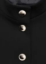 Chaqueta entallada de color negro con cuello mao y cierre frontal de botones metálicos efecto joya. Presenta diseño de largo medio, manga larga y forro interior.