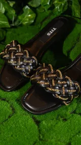 Sandalias negras con tiras trenzadas y cadena dorada.