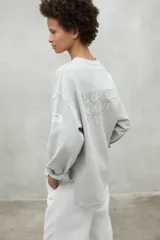 Buzo oversize color gris claro, con cuello redondo, hombros caídos y puños ajustados. Confeccionado con 50% algodón orgánico y 50% algodón reciclado.