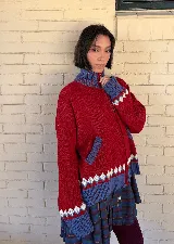 Saco tejido tipo jacquard color bordó con diseño floral en la espalda, cuello alto y cierre frontal de aluminio. Presenta detalles en azul y blanco en el cuello, puños y ruedo, con un patrón geométrico de rombos en la parte inferior.