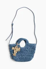 Cartera cruzada en paja trenzada de papel azul con doble asa, cierre magnético y bandolera ajustable, decorada con un dije colgante en forma de pez color beige.