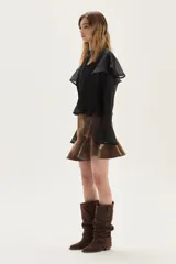 Blusa de manga larga confeccionada en ramio, con diseño de tablas verticales en el frente y la espalda. Presenta cuello alto, cierre frontal con botones y mangas con volados en los hombros y puños acampanados.