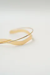 Gargantilla rígida de diseño minimalista en color dorado, compuesta por dos bandas metálicas con forma ondulada que se entrelazan.