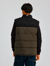 Chaleco acolchado bicolor con diseño de bloques en negro y verde oliva. Presenta cierre frontal completo, cuello alto, bolsillos laterales con cierre y logo de la marca estampado en el pecho.
