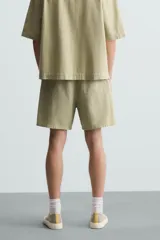 Bermuda de algodón color blanco, de corte relajado (relaxed fit), con cintura elástica ajustable mediante cordón. Posee bolsillos laterales y un bolsillo trasero de plastrón. Presenta un bordado en contraste en la pernera.