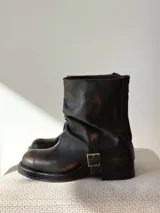 Botas de cuero negro con efecto desgastado en tono marrón, diseño de caña media, punta redondeada, taco bajo y detalle de hebilla metálica lateral.
