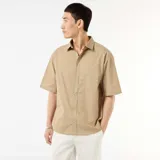 Camisa de manga corta de popelín color beige, con cuello clásico y cierre frontal de botones.