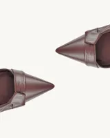 Zapato stileto de cuero color bordeaux, con punta fina, detalle de lazo en el empeine, talón descubierto y tira fina con hebilla.
