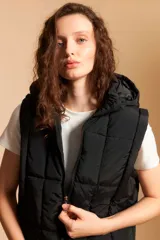 Chaleco puffer negro con capucha y cierre frontal, acolchado con costuras horizontales y verticales.