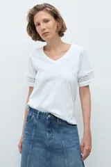Remera blanca de algodón con cuello en V y mangas cortas que presentan un detalle de puntilla en los bordes.