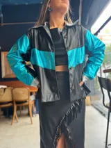 Campera corta de cuerina negra con mangas turquesas metalizadas y detalles plateados en cuello y puños.